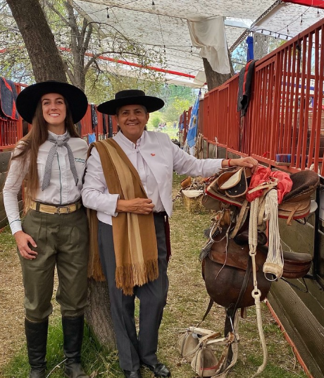 Na foto, duas mulheres, trajadas tipicamente segurando equipamentos para montaria de cavalos.